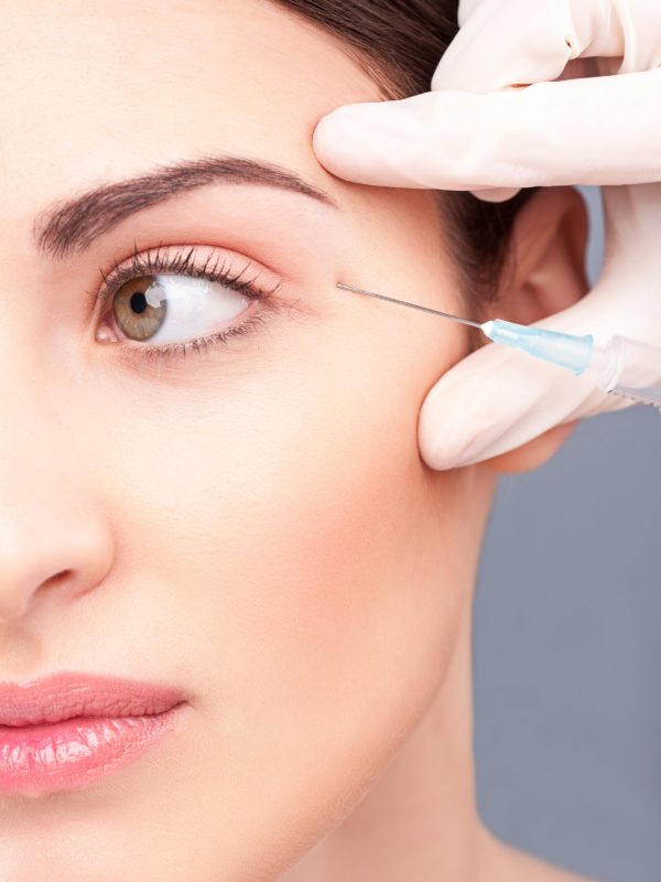 Close up of half of female face. Beautiful girl is receiving botox treatment. Hand of beautician is injecting bottox near her eye