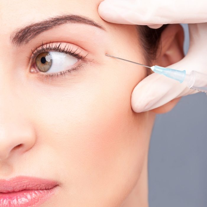 Close up of half of female face. Beautiful girl is receiving botox treatment. Hand of beautician is injecting bottox near her eye